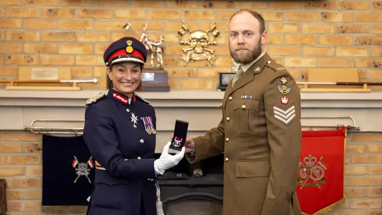 A woman in dark navy ceremonial attire holds up a medal alongside a man in brown ceremonial attire.