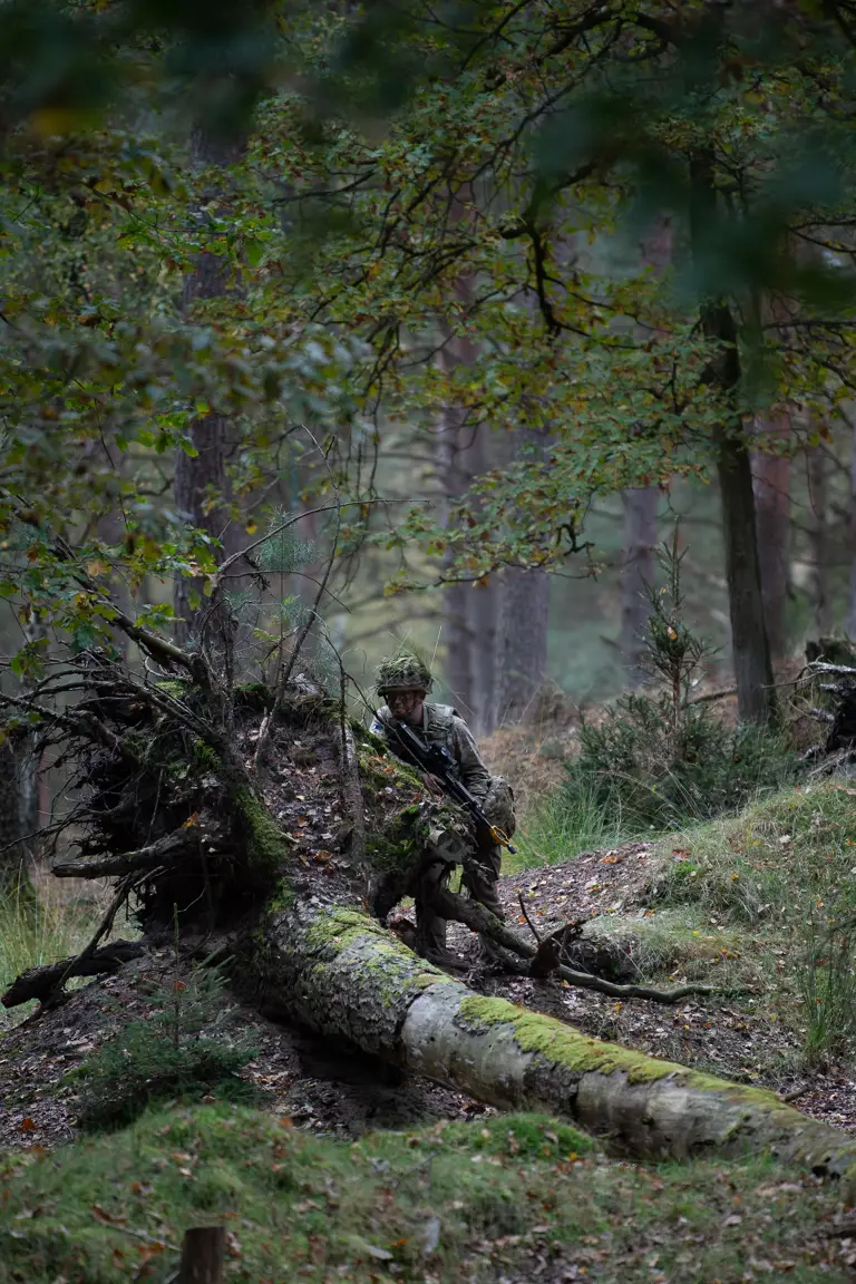 A soldier takes cover behind the roots of an upended tree.