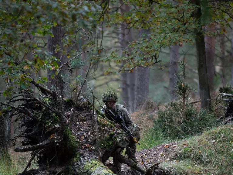 A soldier takes cover behind the roots of an upended tree.