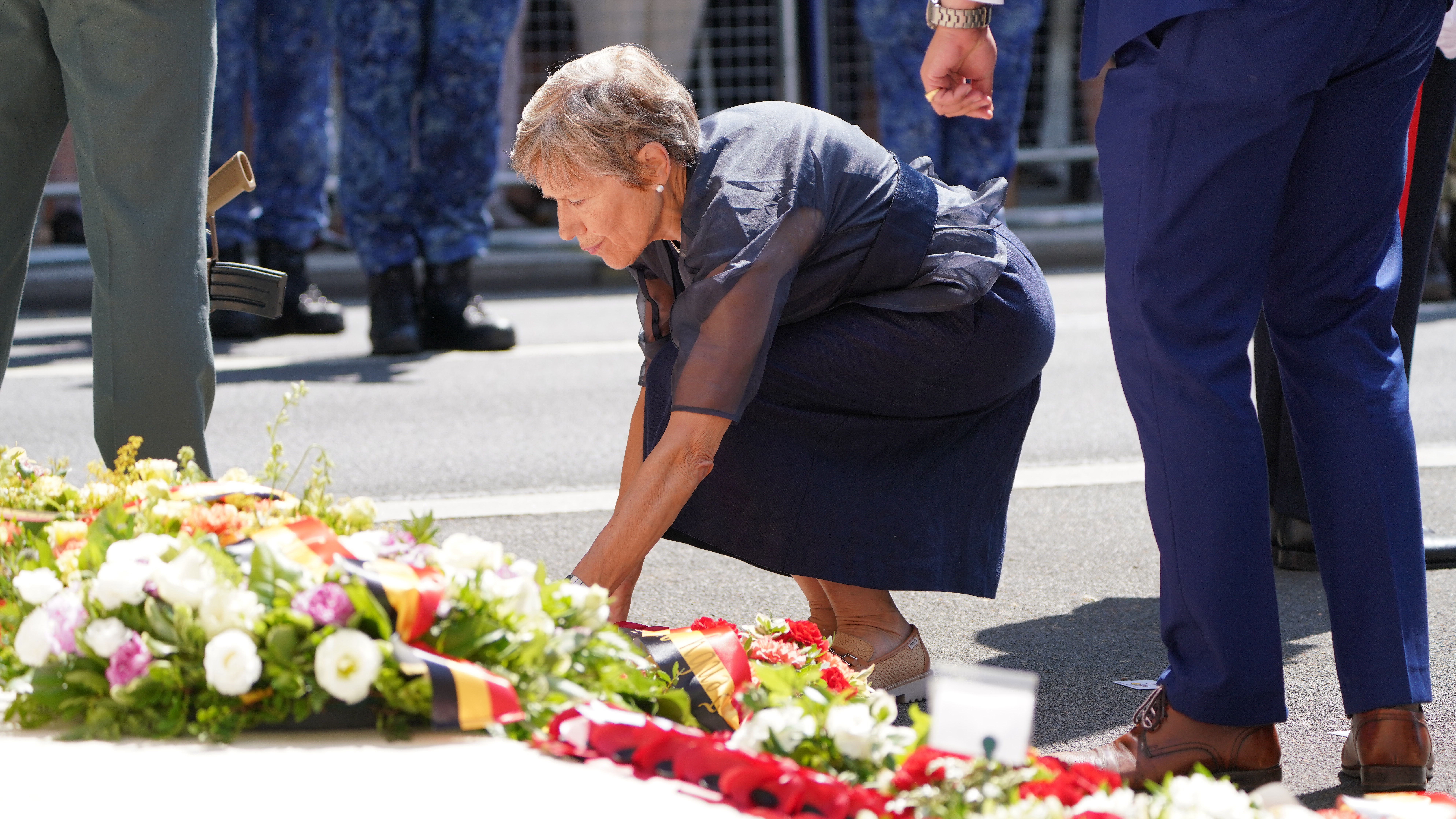 A person is placing a floral arrangement on a street during a ceremonial event, surrounded by others.