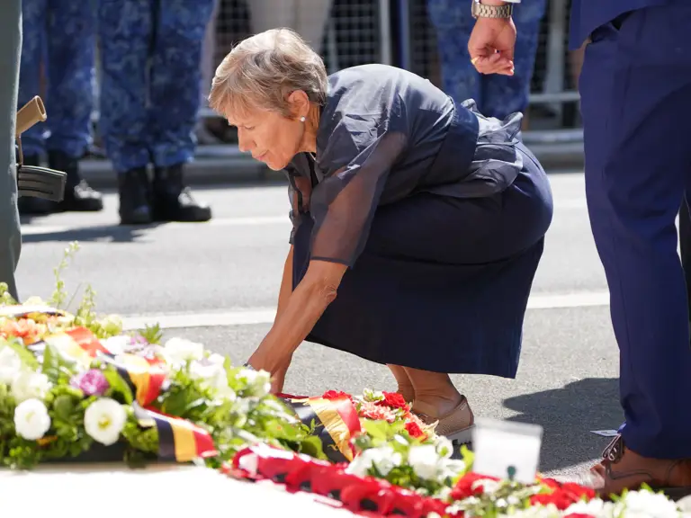 A person is placing a floral arrangement on a street during a ceremonial event, surrounded by others.