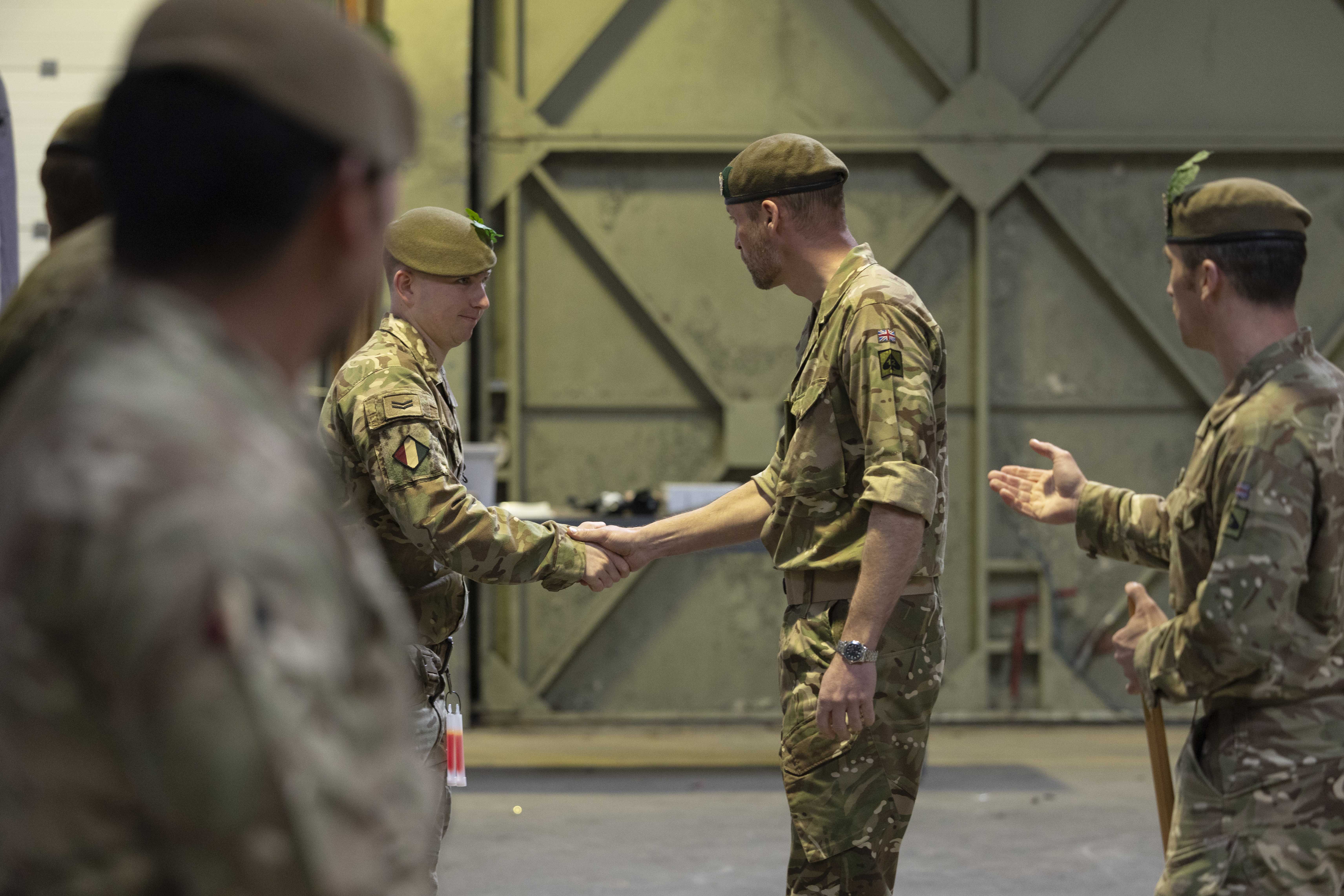 Military personnel in uniform are gathered inside a large industrial space. 