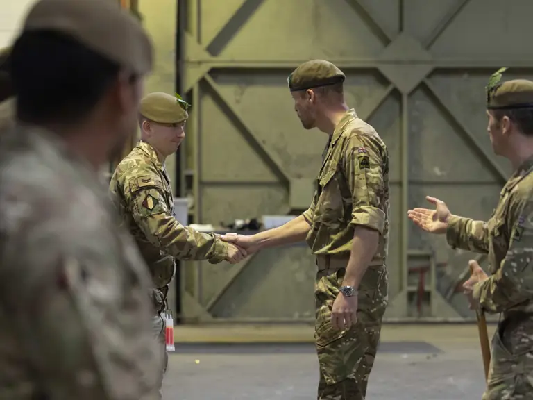 Military personnel in uniform are gathered inside a large industrial space.