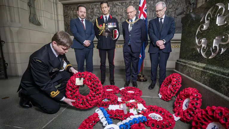 An Australian soldier in black ceremonial uniform lays a wreath in front of four others.