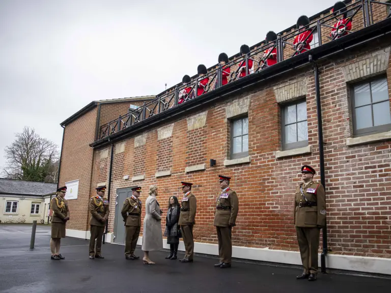 Her Royal Highness The Duchess of Edinburgh is greeted soldiers in khaki uniforms. Behind them is a brick built building