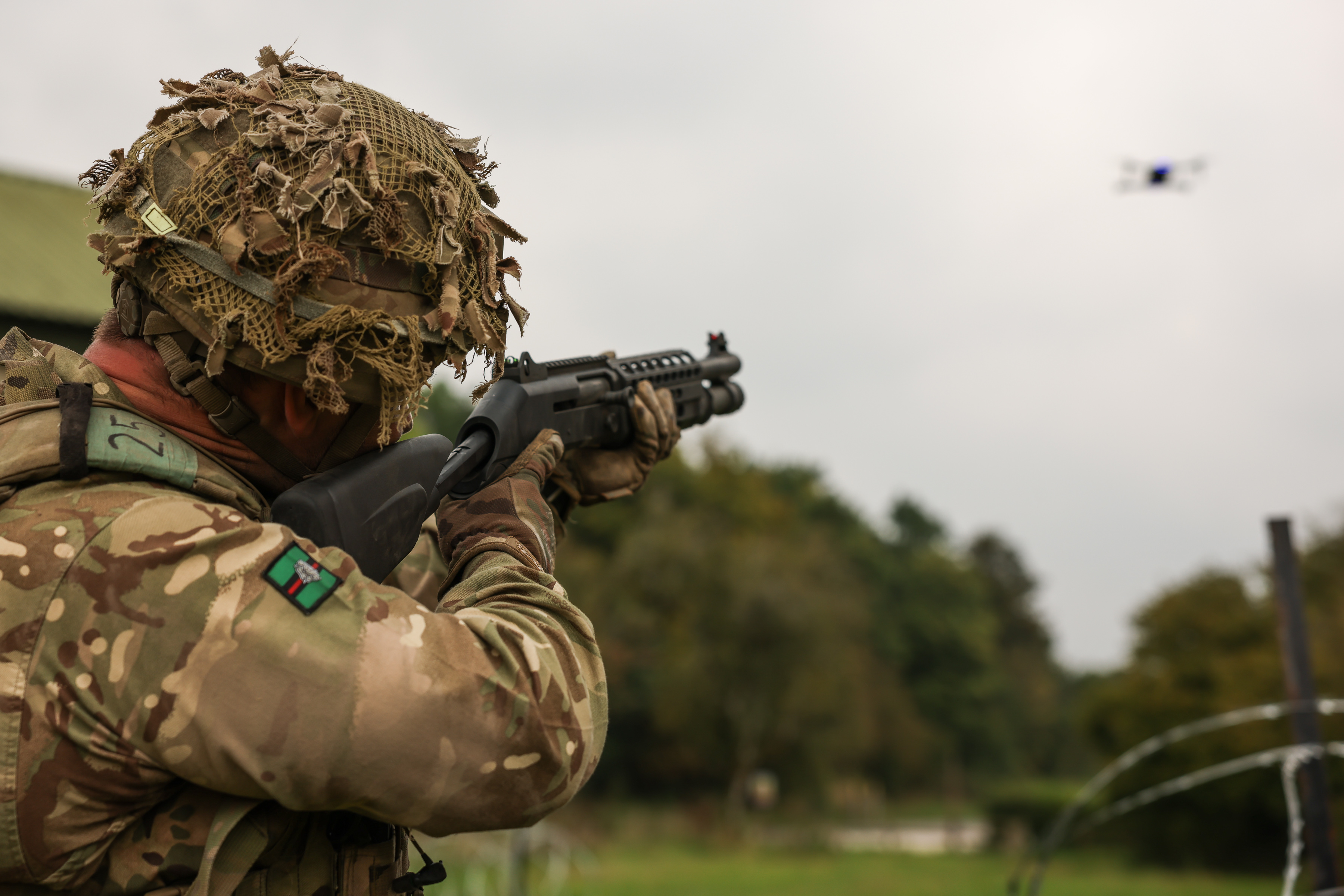 A soldier in uniform points a gun at a drone. 