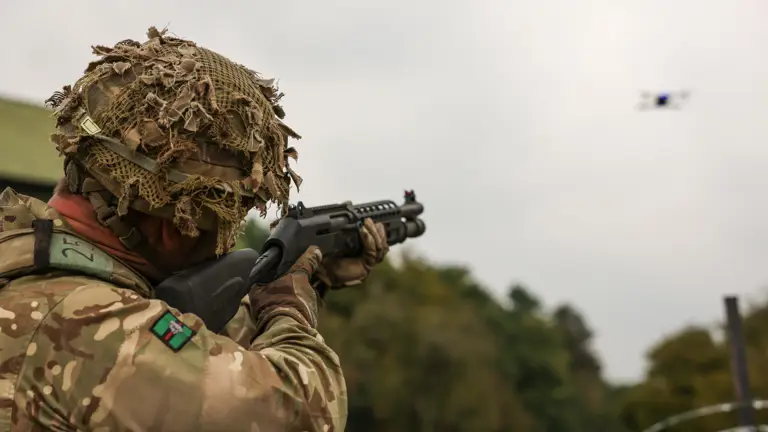 A soldier in uniform points a gun at a drone.