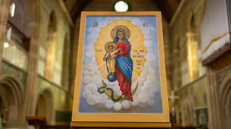 Icon of Our Lady of Victories holding a child, surrounded by clouds and radiant light inside a church.