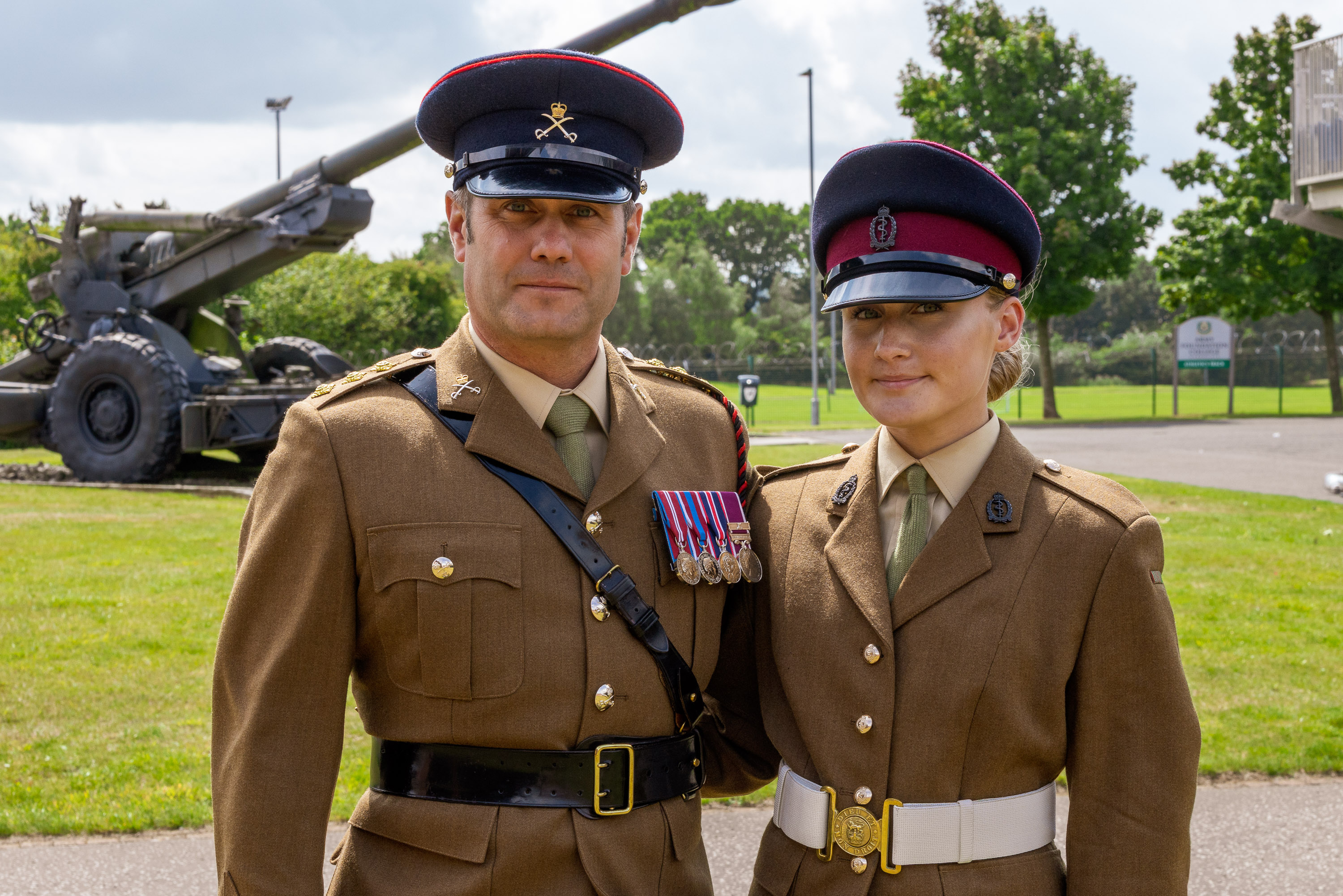 Madalyn is photographed wearing her brown uniform with her navy cap on her head. Her father Graham is photographed to her right wearing his brown uniform and peak cap with his medals mounted on his chest. They are both seen smiling with their arms around each others back.