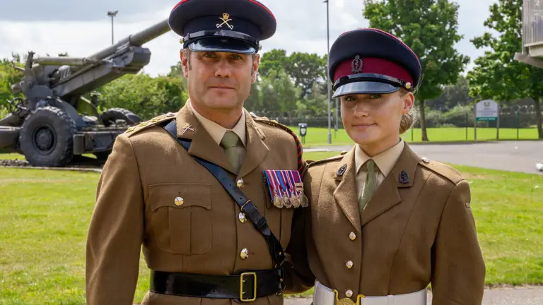 Madalyn is photographed wearing her brown uniform with her navy cap on her head. Her father Graham is photographed to her right wearing his brown uniform and peak cap with his medals mounted on his chest. They are both seen smiling with their arms around each others back.