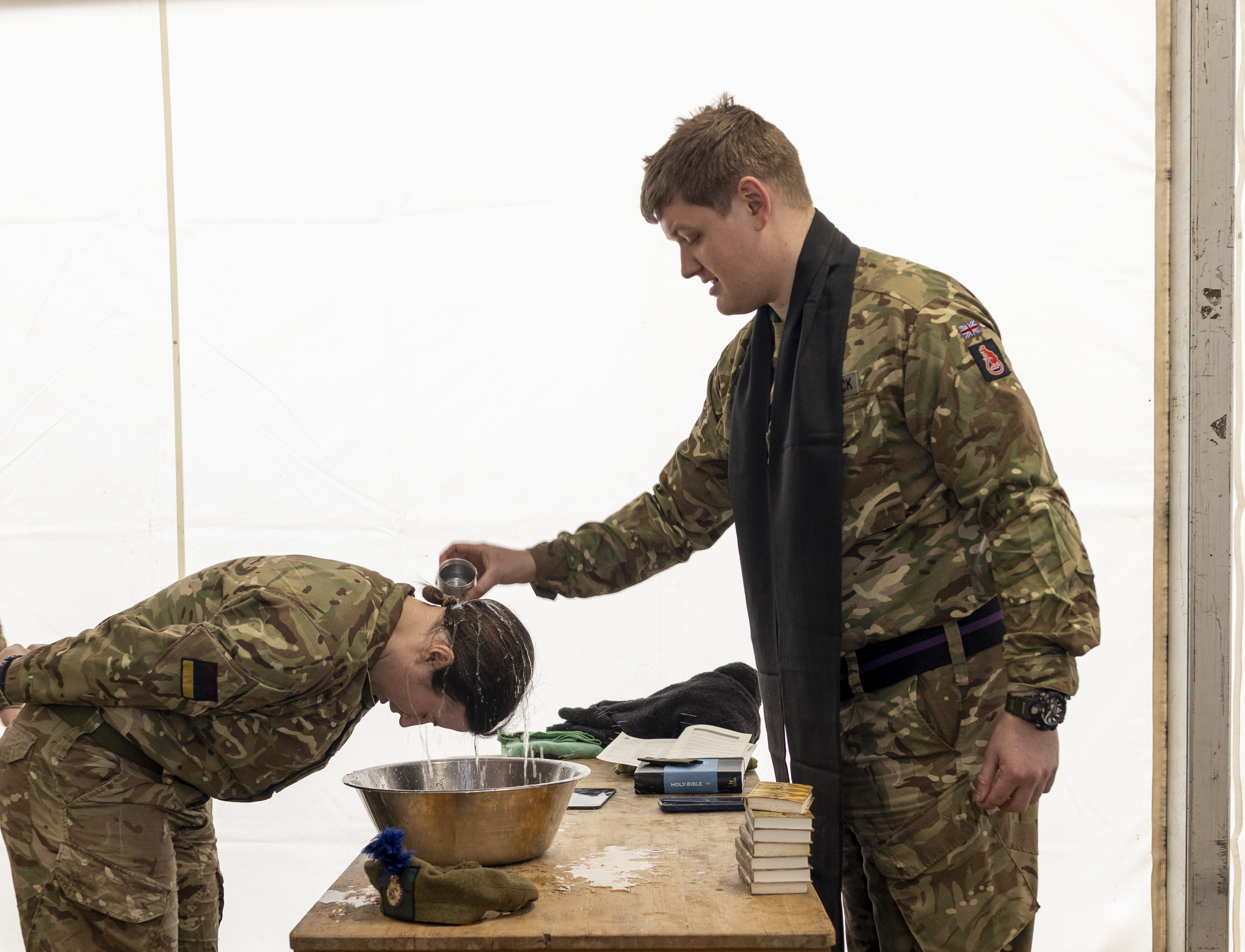 A woman in uniform has water poured over her head by a padre in Uniform during a baptism. 
