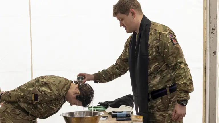 A woman in uniform has water poured over her head by a padre in Uniform during a baptism.