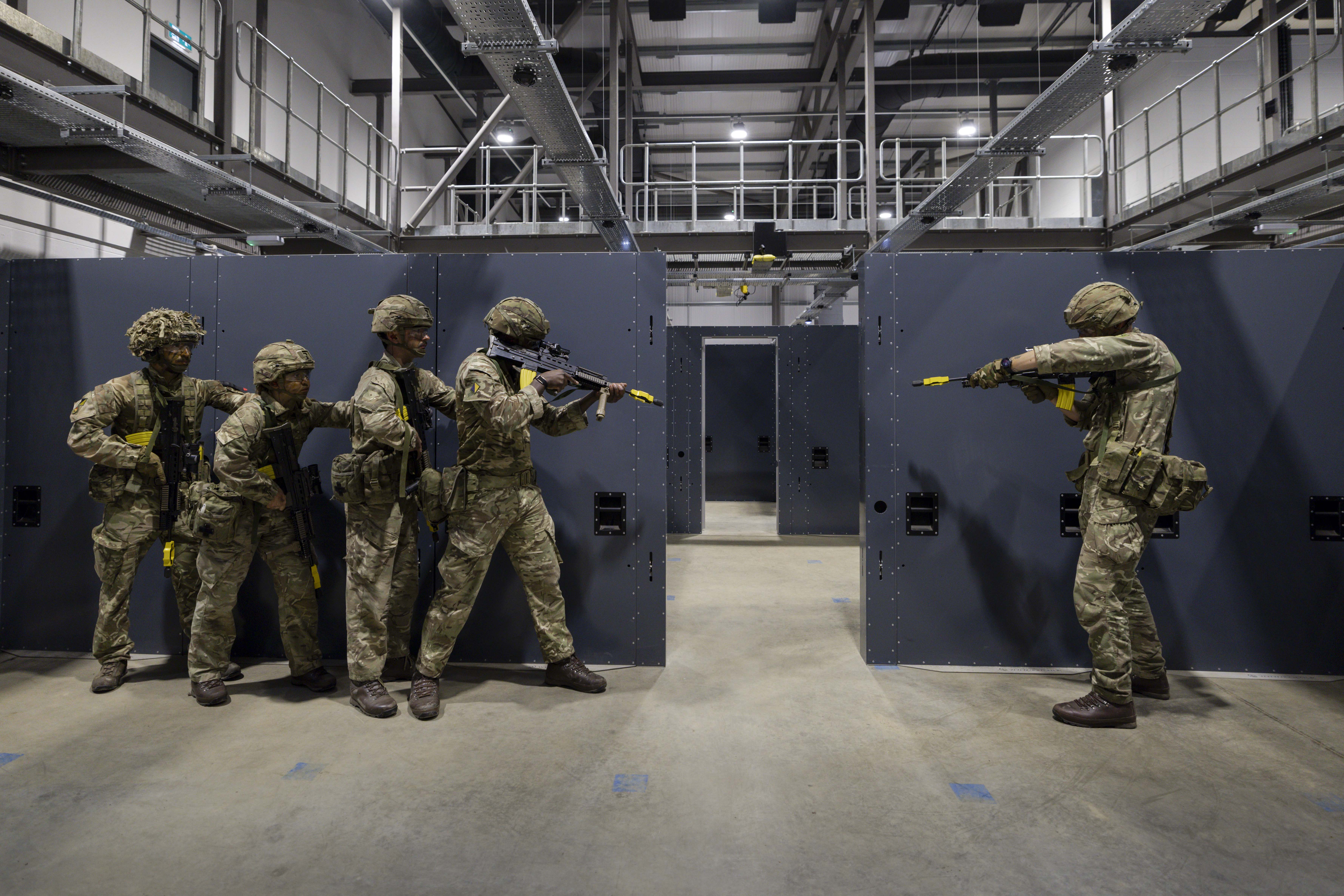 Soldiers in camouflage uniforms holding rifles stand ready in concrete building 