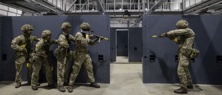 Soldiers in camouflage uniforms holding rifles stand ready in concrete building