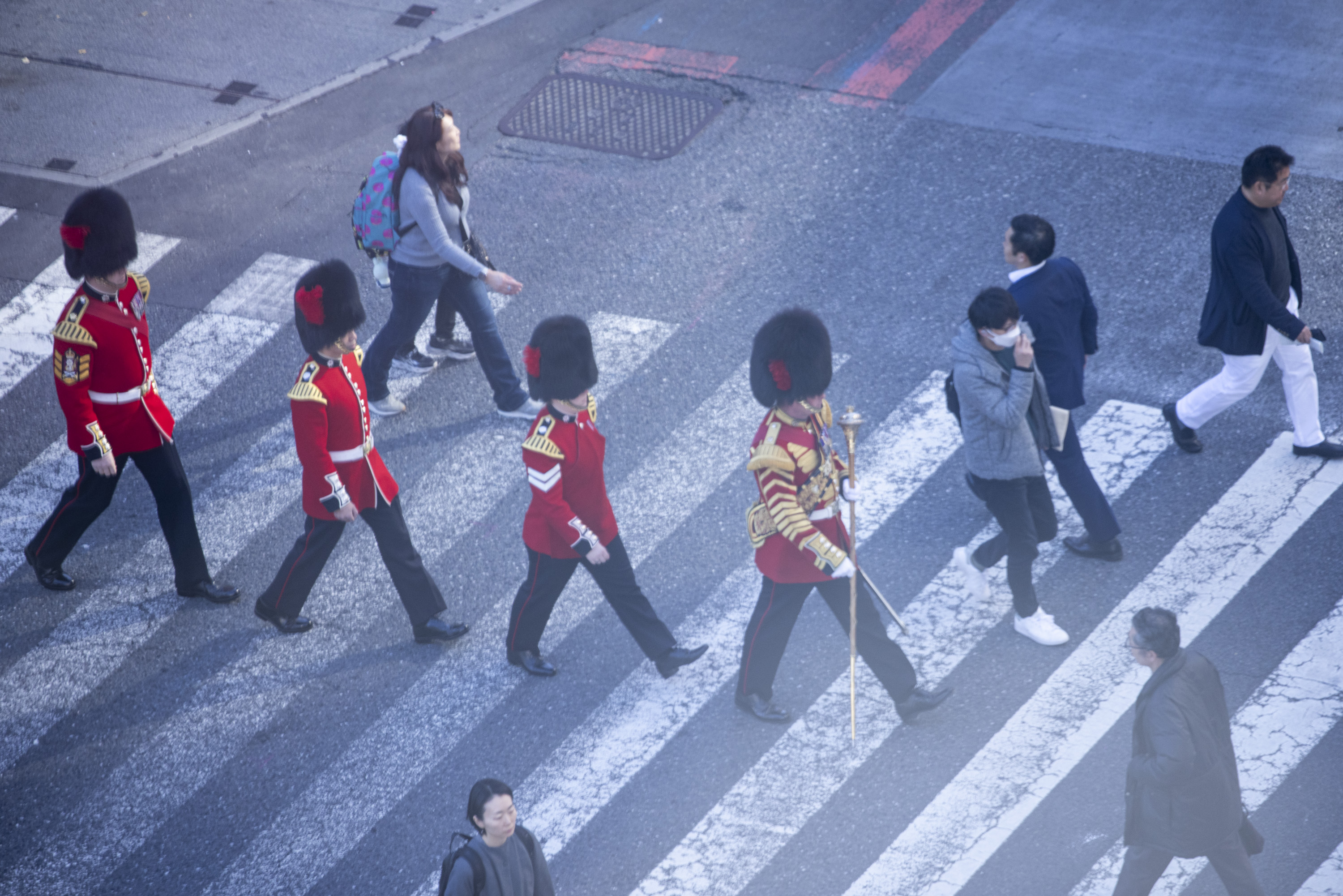 Four soldiers in red tunics and bearskin hats are pictured at a busy crossing in Japan. 
