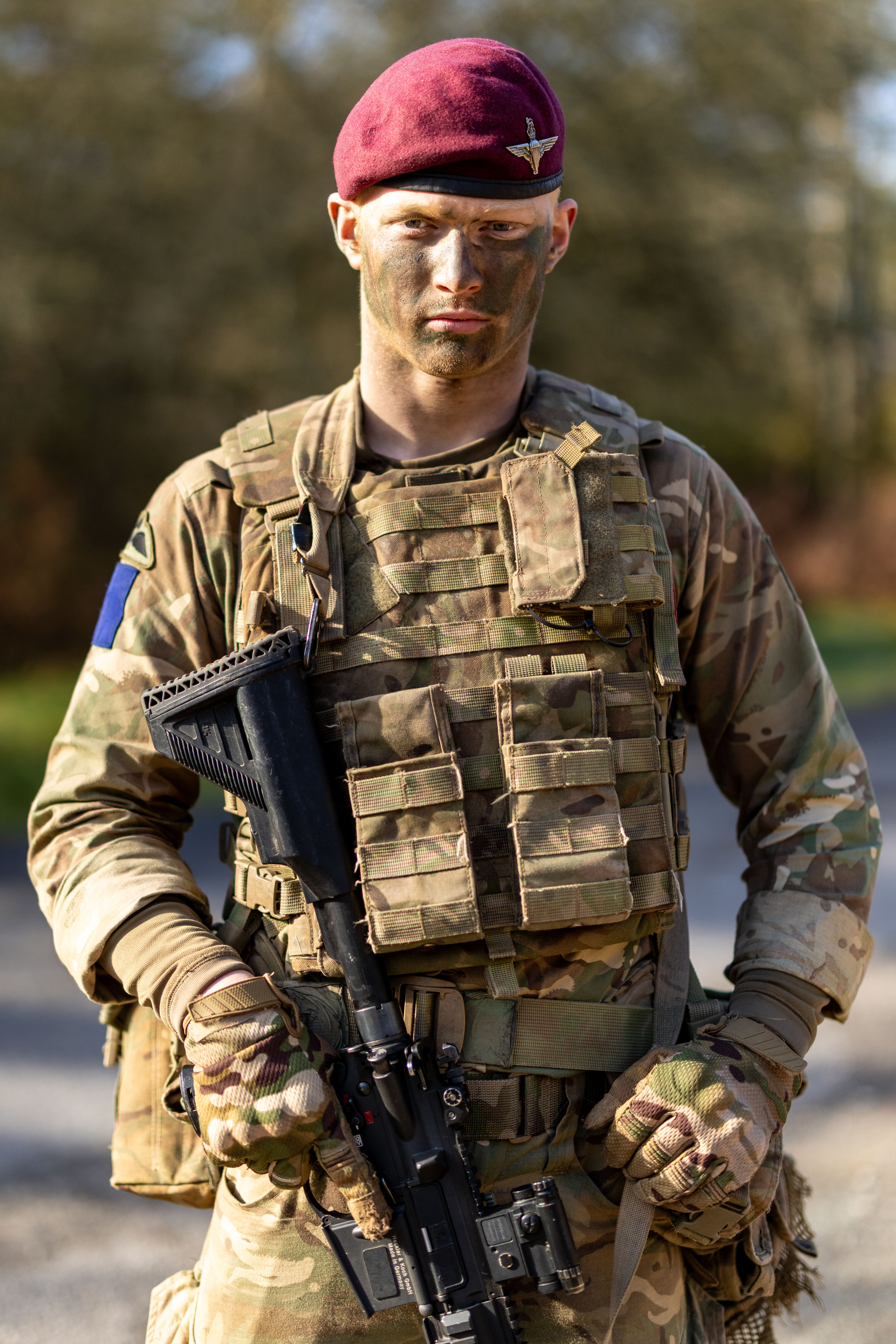 The image shows a person in military camouflage attire, wearing a maroon beret with an emblem. 