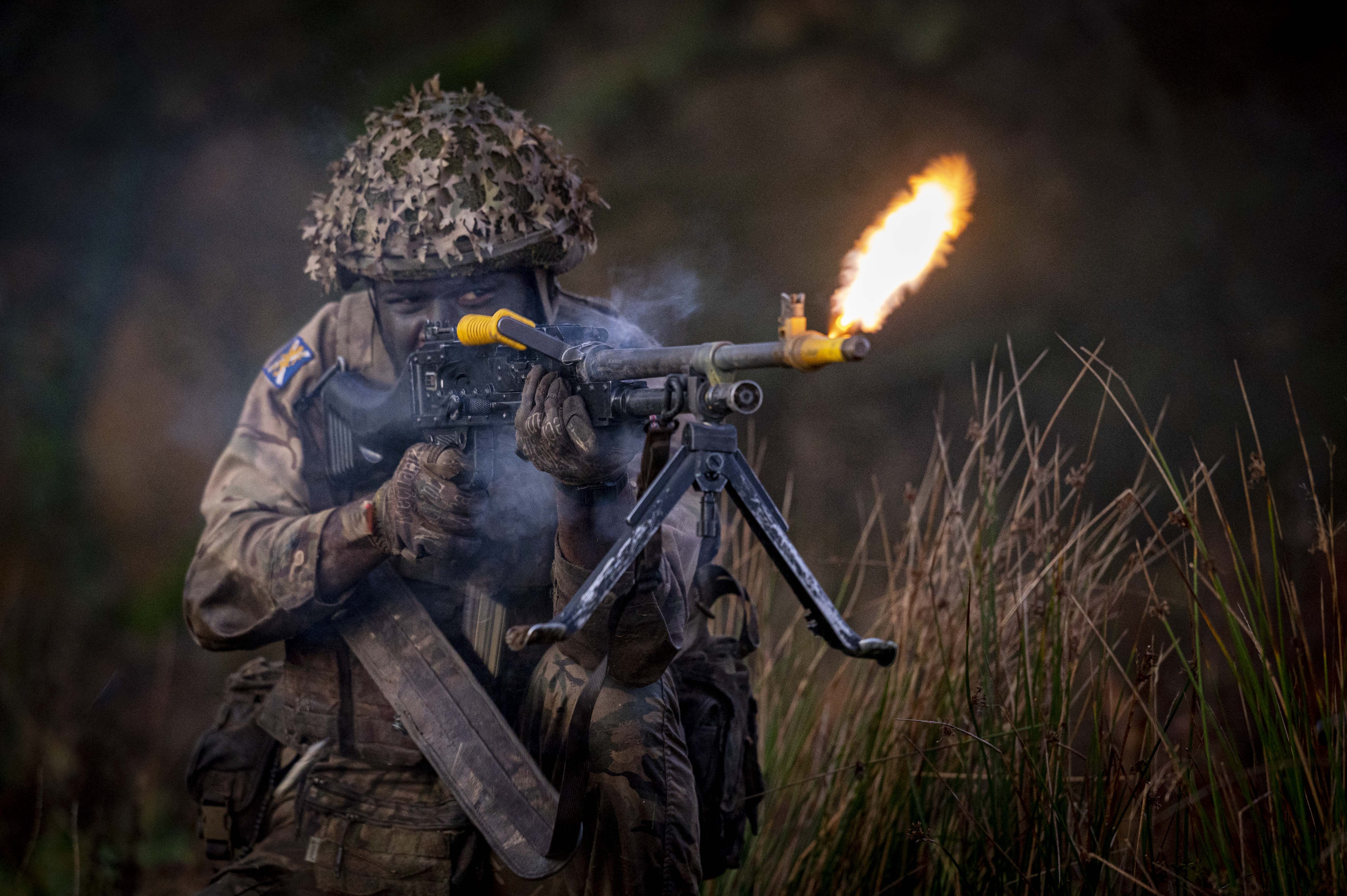 A soldier wearing camouflage uniform fires a rifle.
