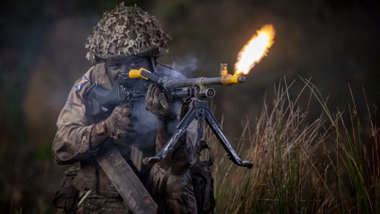 A soldier wearing camouflage uniform fires a rifle.