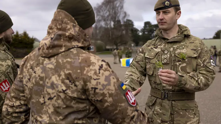 A man in Ukrainian Army uniform is handed a shamrock by a man in a British Army uniform.