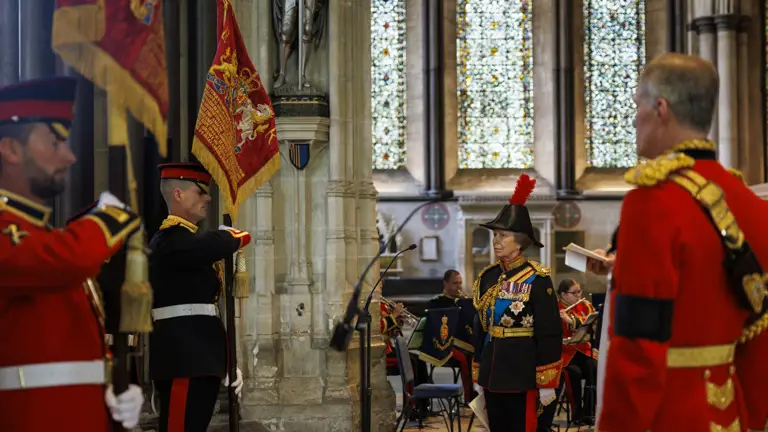 Two people dressed in military ceremonial uniform. They are holding ceremonial flags.