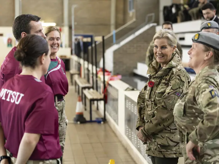 Two groups, one in maroon MTSU shirts and the other in camouflage military uniforms, stand facing each other.