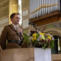 A military officer in uniform stands behind a stone lectern adorned with a colorful floral arrangement inside a church.
