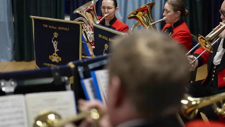 A brass band in red and black uniforms plays with focus and precision.
