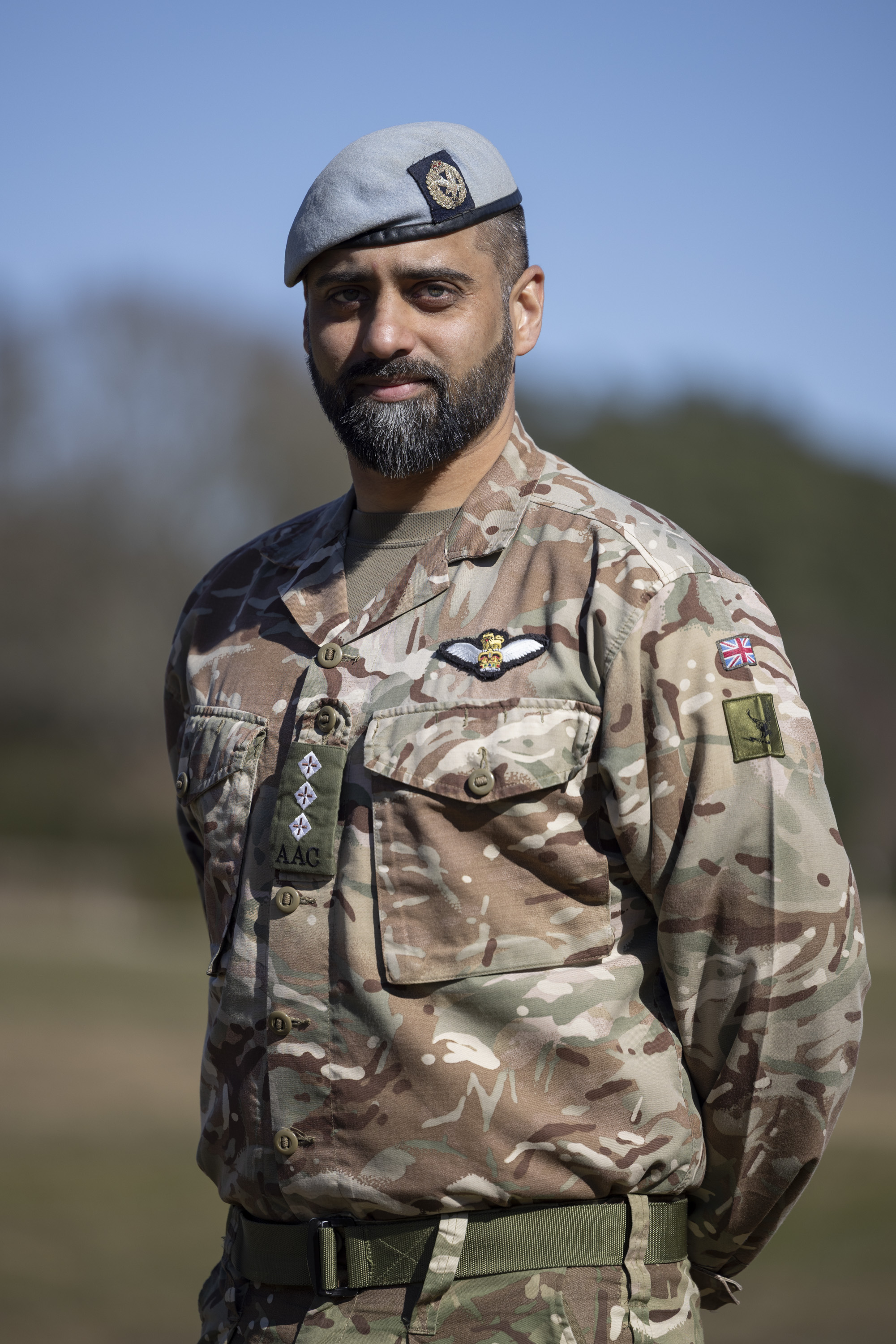 Soldiers in his camouflage unifrom with his arms behind his back and light blue berets on their heads stood outside.