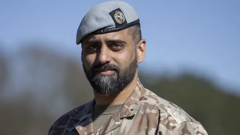 Soldiers in his camouflage unifrom with his arms behind his back and light blue berets on their heads stood outside.