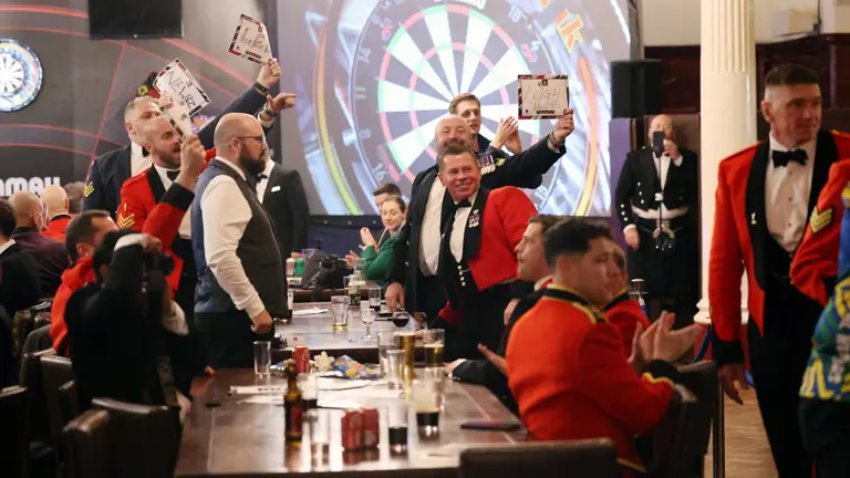 Group of people in formal attire celebrating and holding up scorecards in a lively darts competition setting.