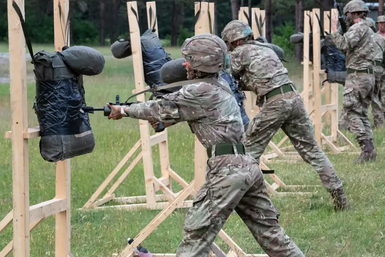Officer Cadets in camouflage uniform conducting bayonet drills with training dummies held up on wooden frames