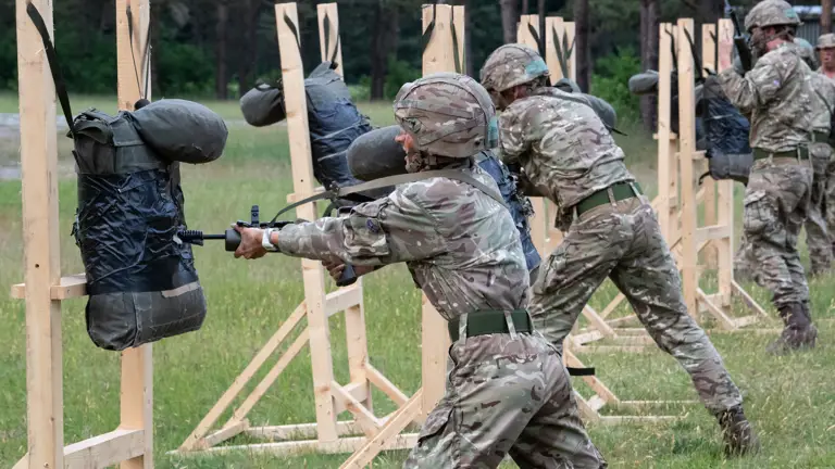Officer Cadets in camouflage uniform conducting bayonet drills with training dummies held up on wooden frames
