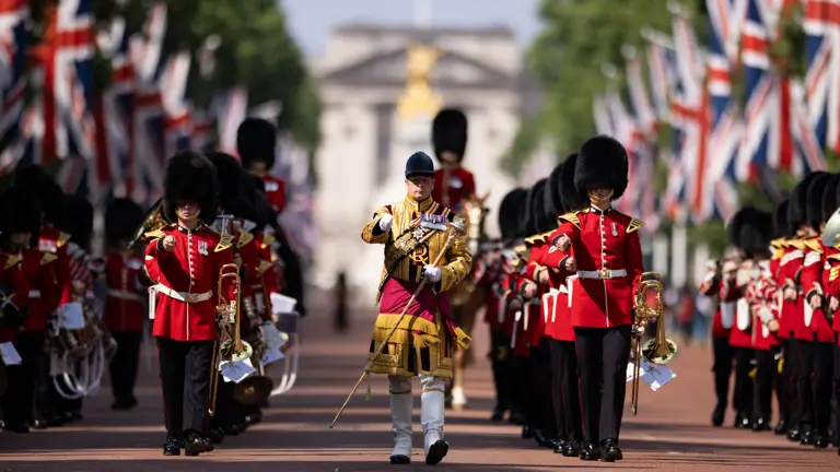 Four lines of soldiers in red ceremonial attire march behind a soldier in yellow ceremonial attire.