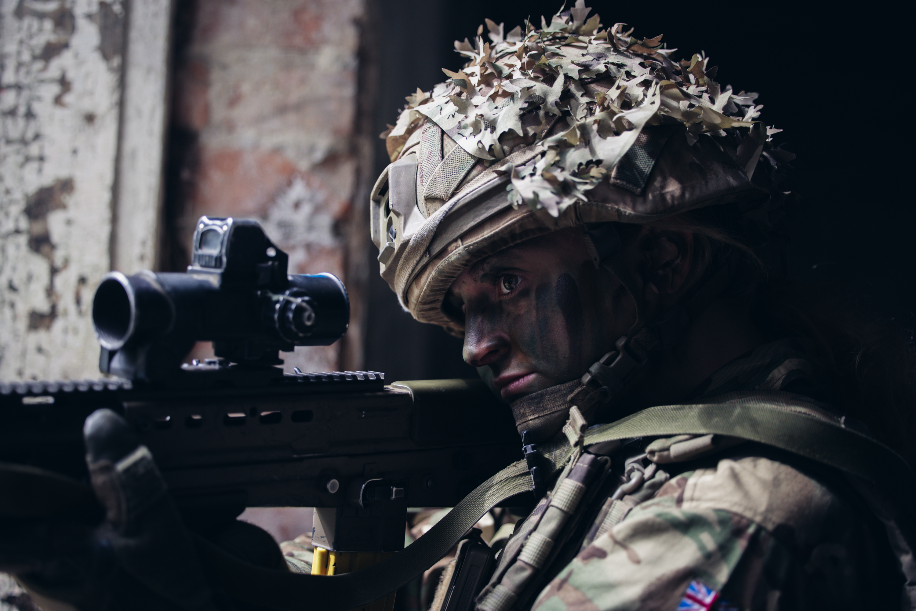 A soldier takes aim with her weapon, pointing it outside from a window.