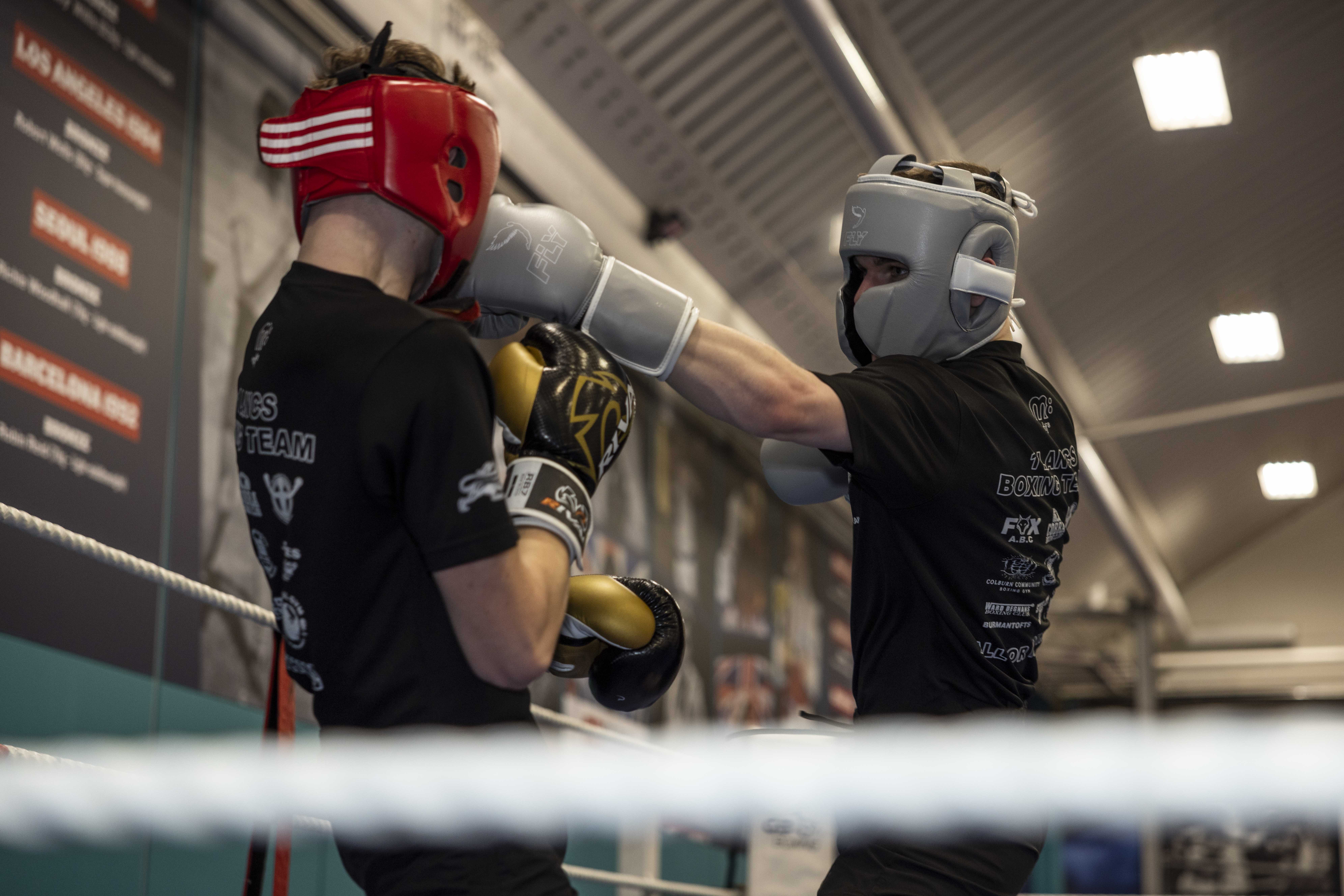 A man wearing a black top and silver hat and gloves punches a man wearing a black top and red hat.