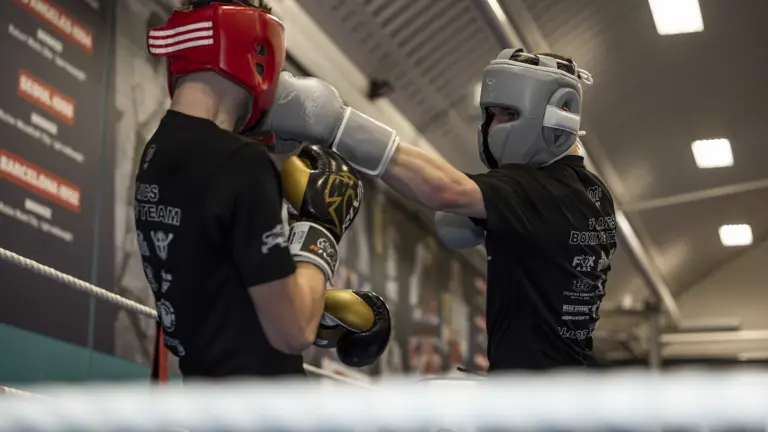 A man wearing a black top and silver hat and gloves punches a man wearing a black top and red hat.