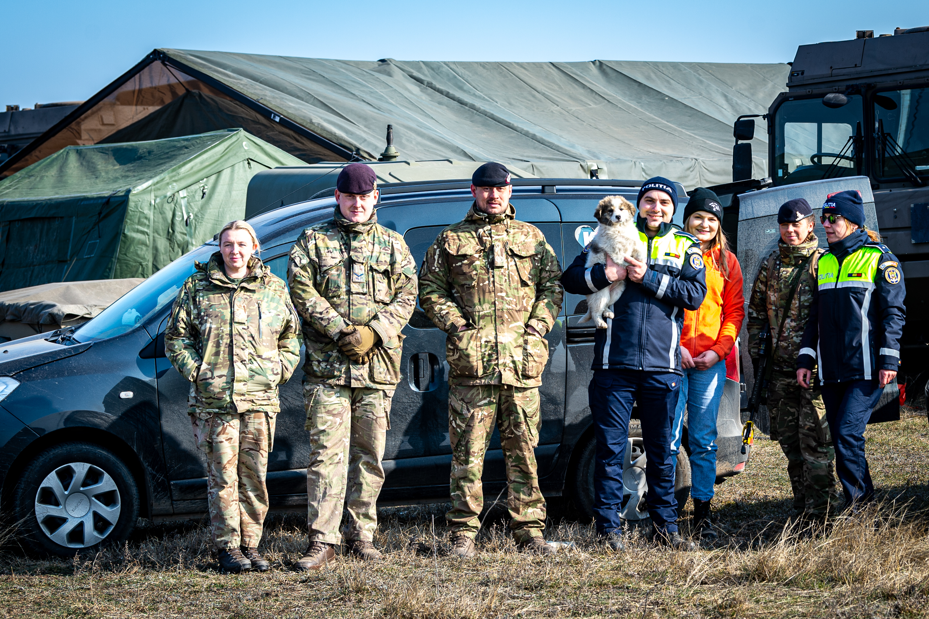 A combination of British military personnel and Romanian police officers are pictured with a puppy.