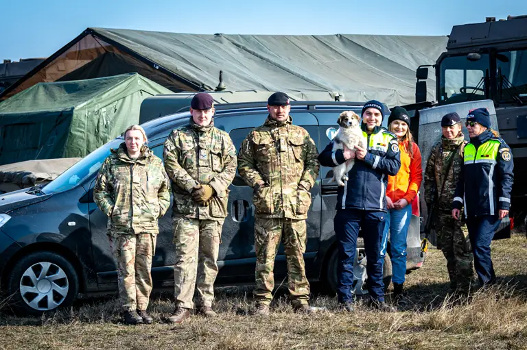 A combination of British military personnel and Romanian police officers are pictured with a puppy.