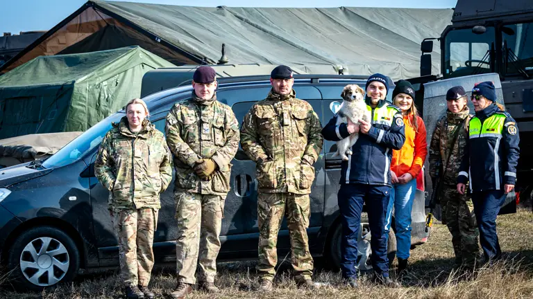 A combination of British military personnel and Romanian police officers are pictured with a puppy.