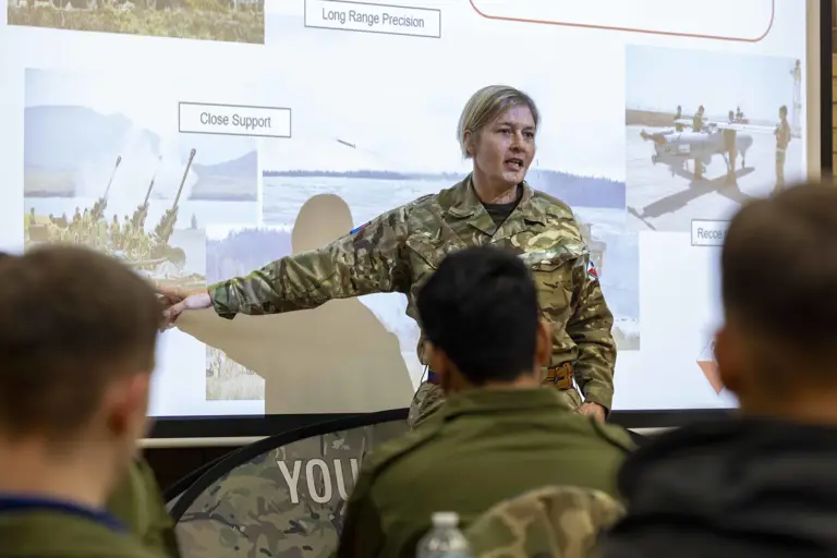Military instructor in camouflage uniform pointing at a presentation slide.