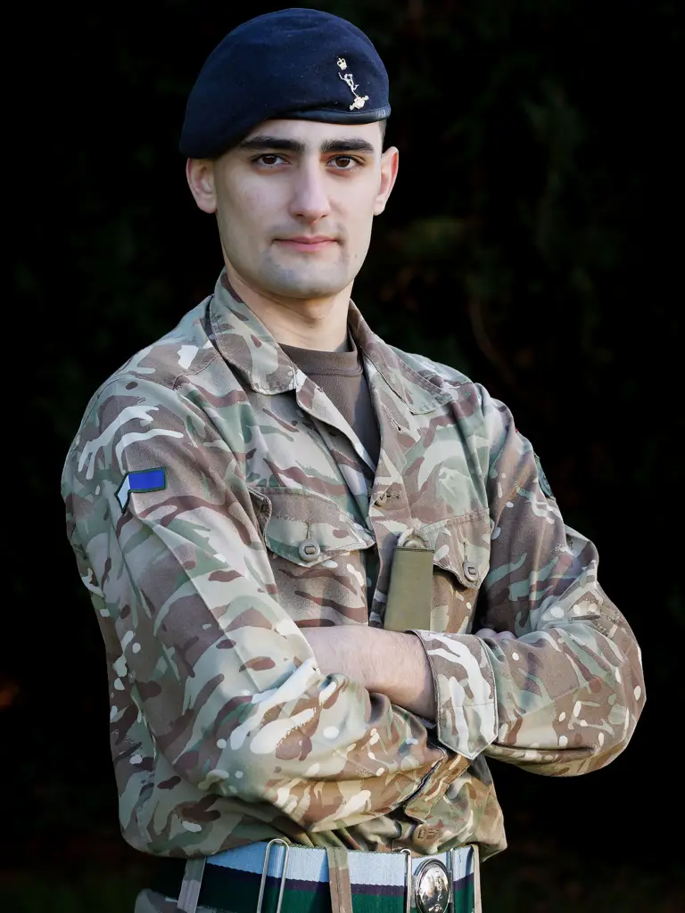 Soldier in camouflage uniform and beret stands confidently with arms crossed against a dark backdrop, exuding strength and determination.