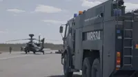 Image shows an AH64E Apache Helicopter stationary on the ground being refuelled by army air corps soldiers. A large Army vehicle is positioned on the right in the foreground.