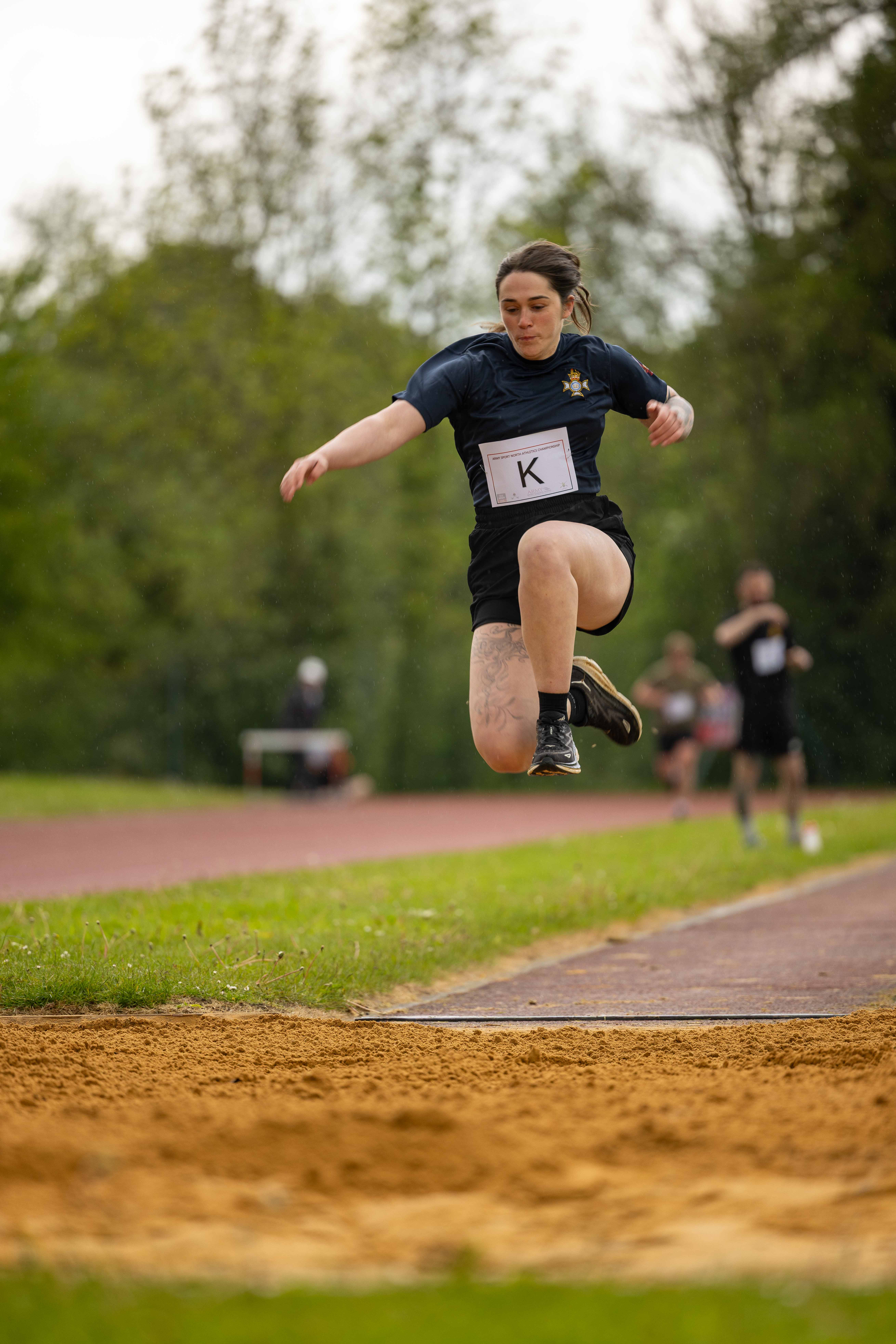 An athlete is performing a long jump on an outdoor track. The ground is covered with sand.