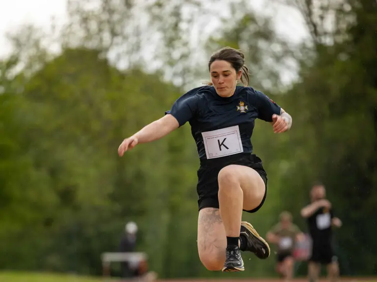 An athlete is performing a long jump on an outdoor track. The ground is covered with sand.