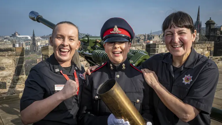 Gunner Caroline Gallagher is stood next to Watched by her fire crew and crew friends Shereen Hasham (Right) and Lindsay Hopper (Left) dressed in No.1 uniform dress holding an empty shell from the gun salute.