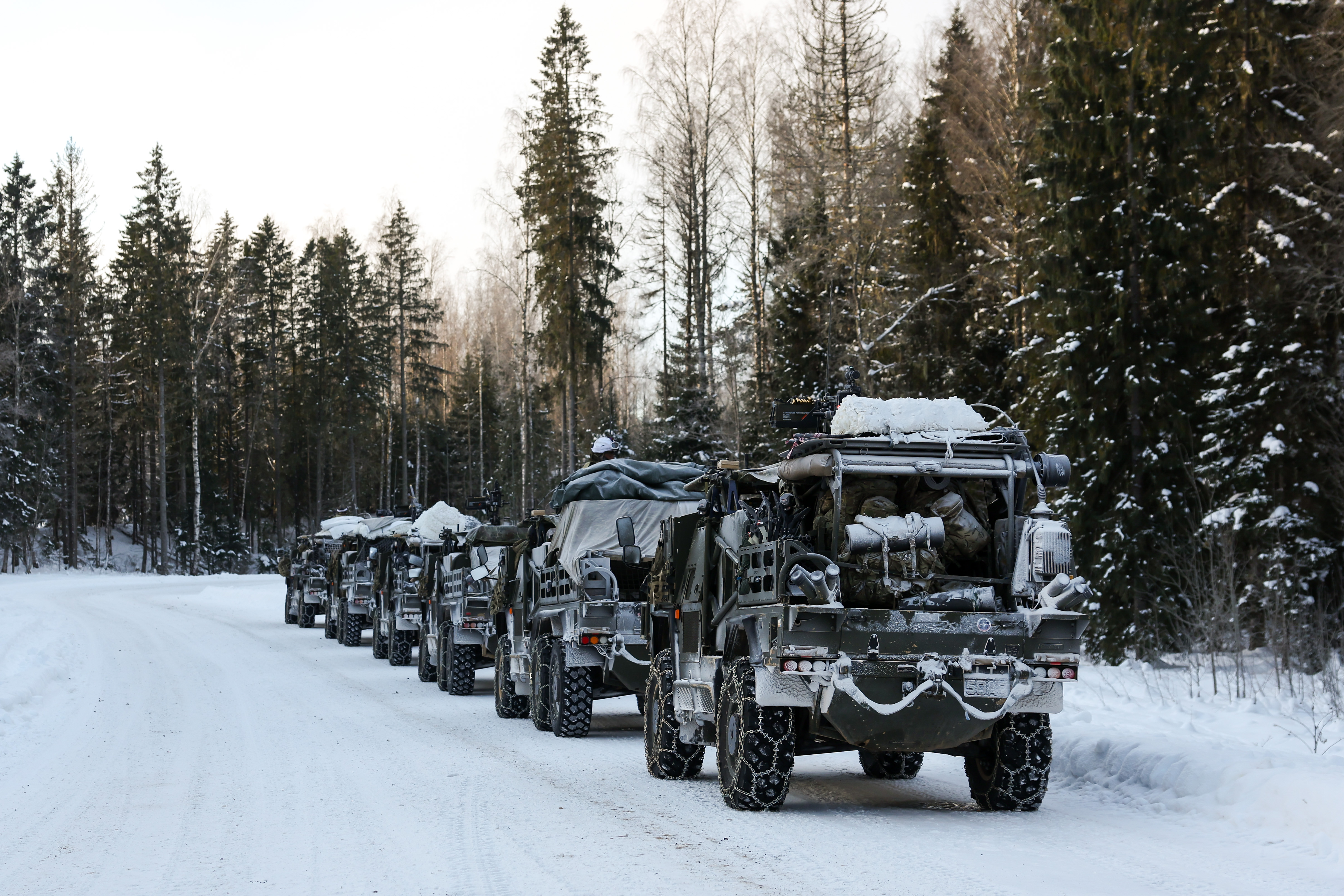 A convoy of military vehicles covered in snow parked along a snowy forest road during winter.