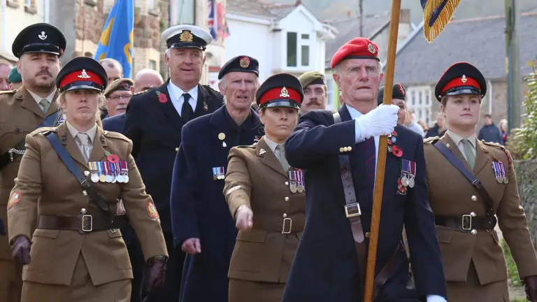 Three female soldiers march in brown ceremonial uniforms at the start of a parade.