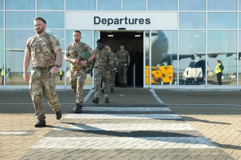 Soldiers in uniform are pictured leaving an airport with the departure sign overhead. 