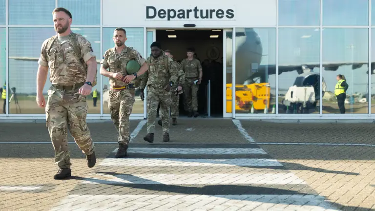 Soldiers in uniform are pictured leaving an airport with the departure sign overhead.