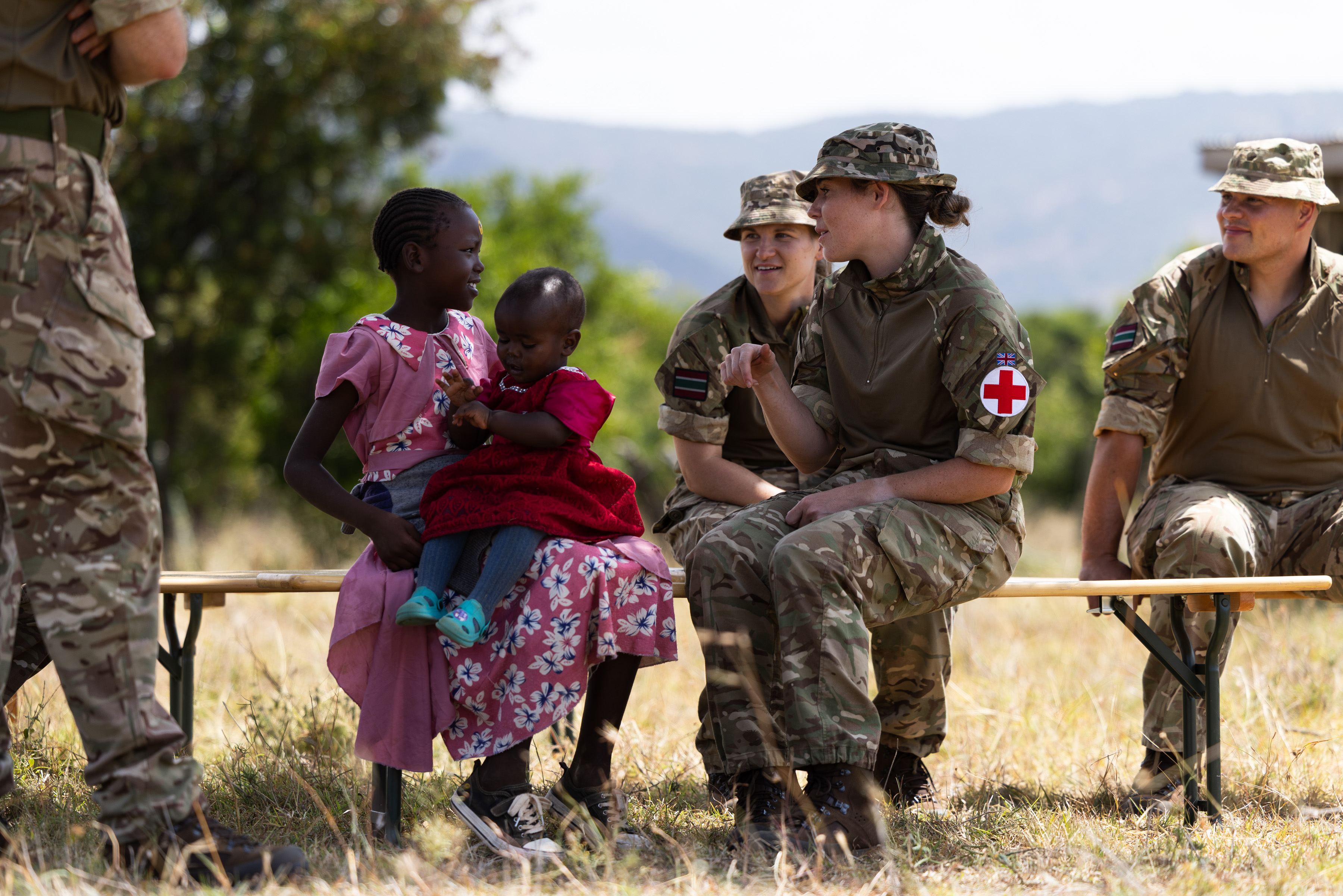 Several people in military uniforms sit on a bench in a grassy area. 